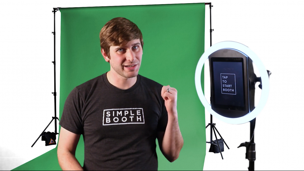 man standing in front of green screen backdrop standing next to simple booth halo photo booth