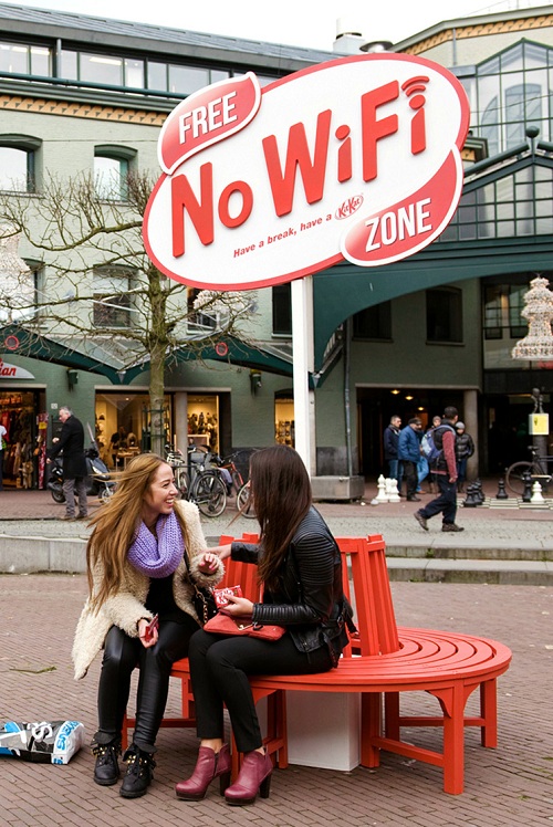 Women talking and sitting on bench under Free No Wifi Zone signage