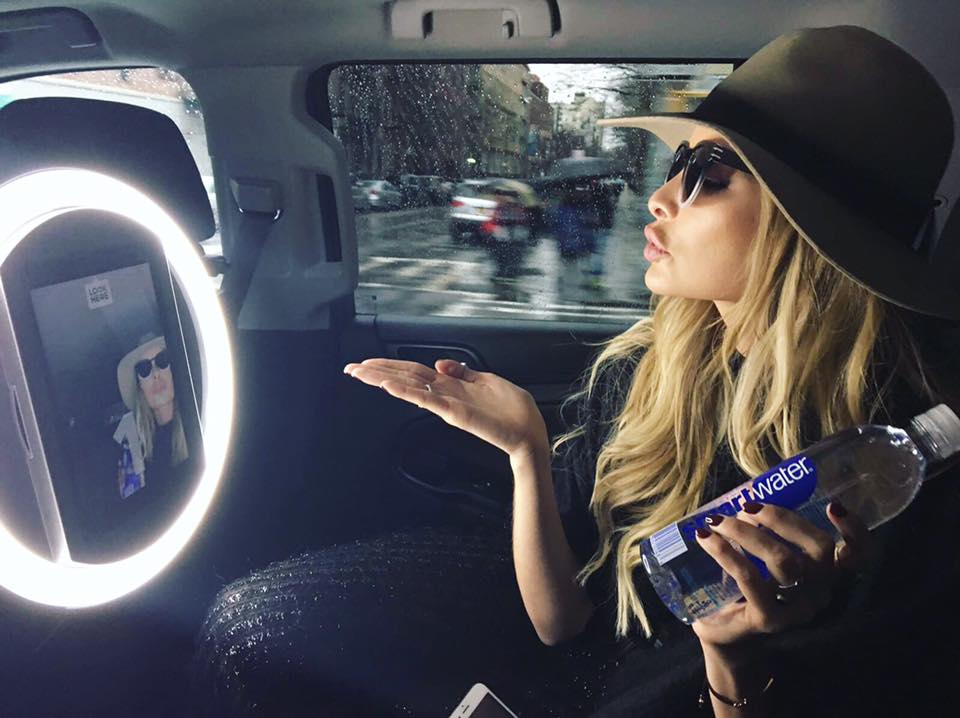 Influencer in Uber taking a selfie with a HALO selfie station and blowing. a kiss