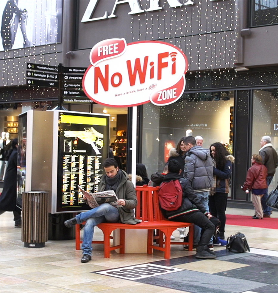 Man reading paper on bench under Free No Wifi Zone signage